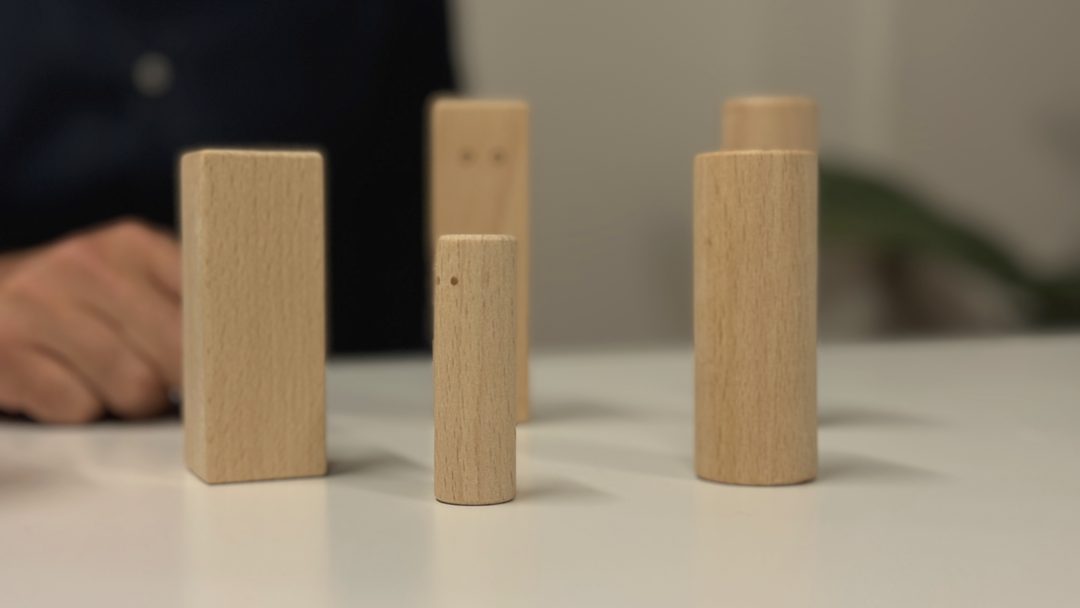 Figuras de madeira sobre uma mesa clara, uma mão a mover uma delas.