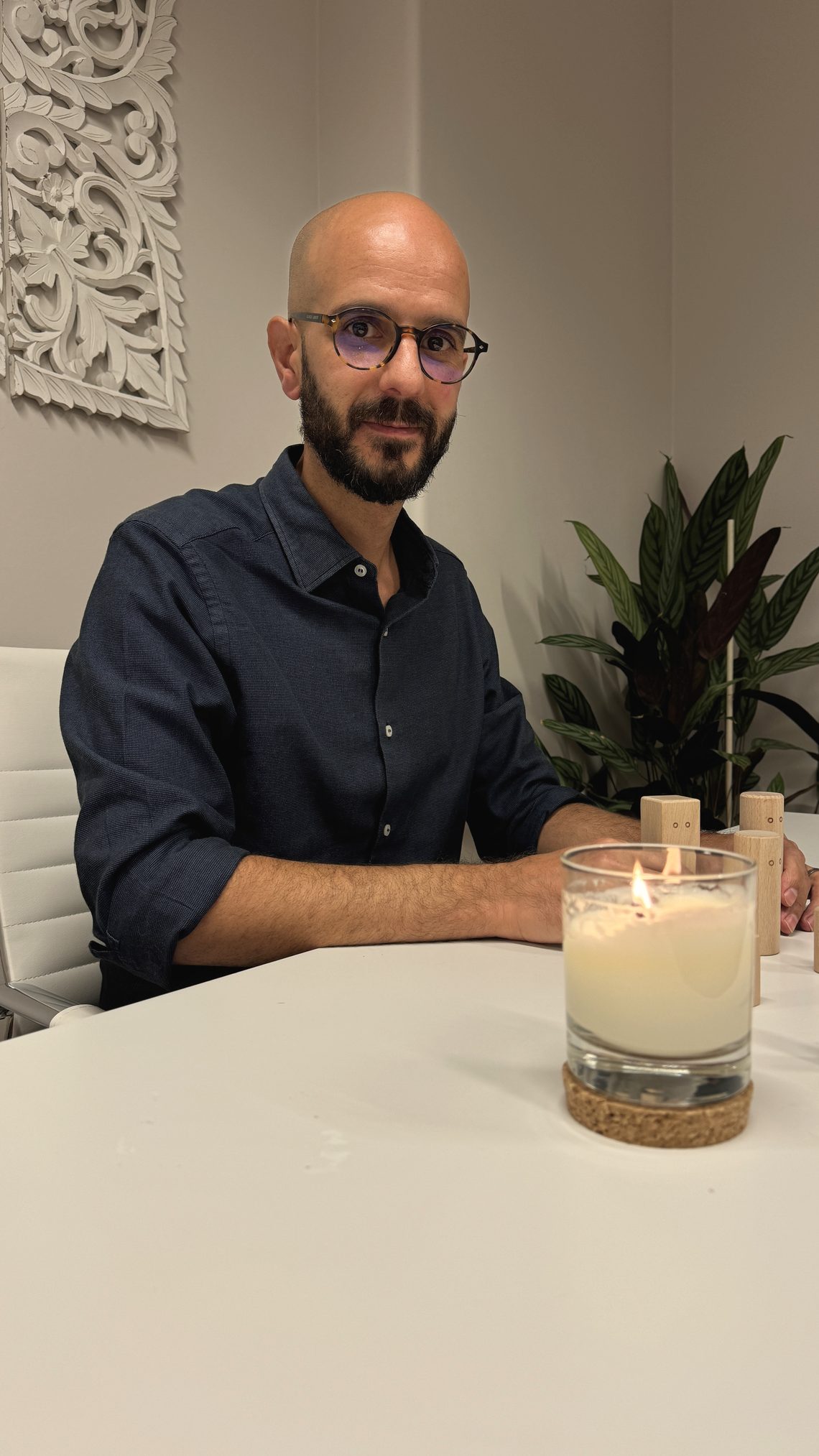 Rodrigo Justo, sentado a uma mesa clara com uma vela acesa e figuras de madeira, olhar calmo.